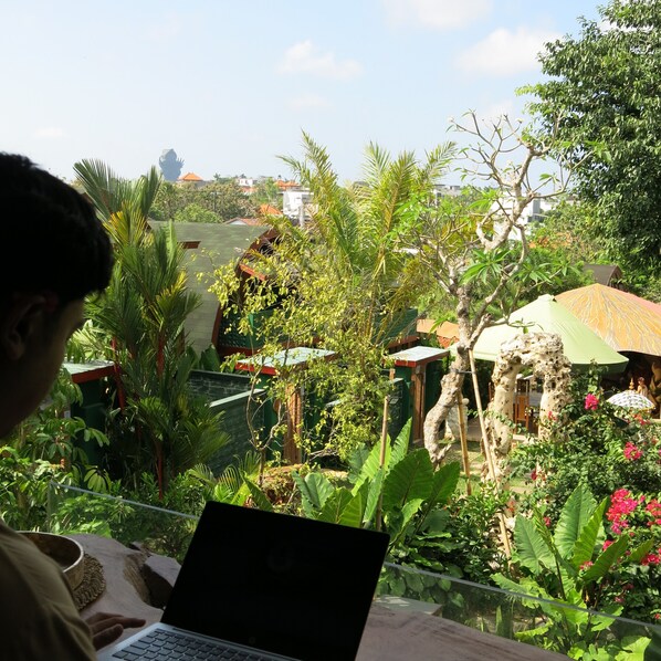 A person using a laptop with a view of a garden and a building in the background.