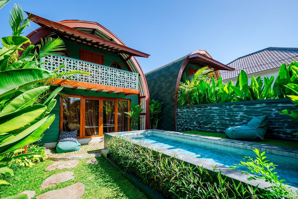A modern house with a swimming pool, surrounded by lush greenery and a stone wall.