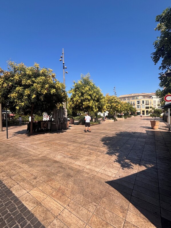 A spacious public square with a tiled floor, trees, and a building in the background.