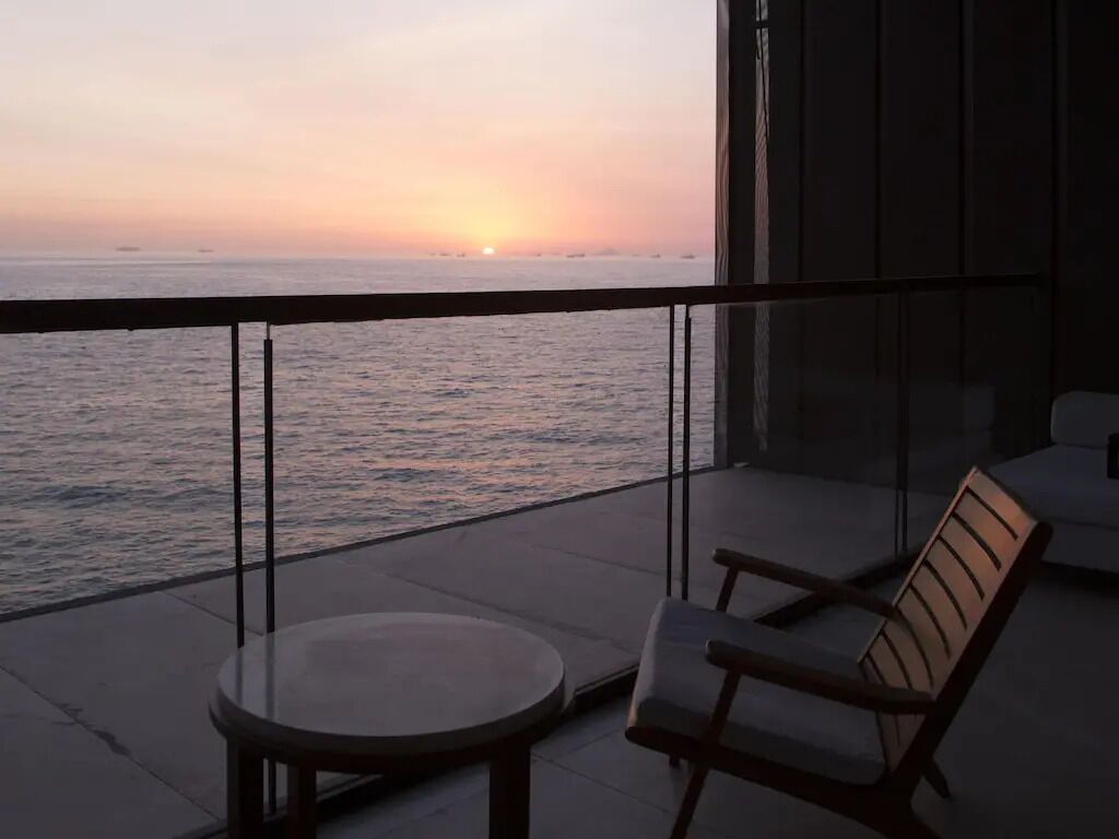 Un balcon avec vue sur la mer au coucher du soleil, une table ronde et deux chaises.