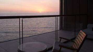 Un balcon avec vue sur la mer au coucher du soleil, une table ronde et deux chaises.