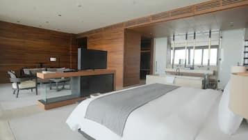 A modern hotel room with a large bed, a desk with a flat-screen TV, a mirror, and a wardrobe.