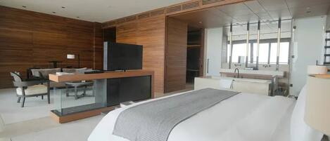 A modern hotel room with a large bed, a desk with a flat-screen TV, a mirror, and a wardrobe.
