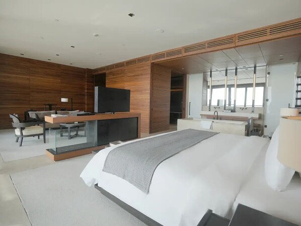 Quarto de hotel moderno com uma cama grande, uma mesa de trabalho com televisão de tela plana, um espelho e um guarda-roupa.