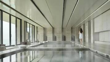 A spacious indoor swimming pool with clear glass walls, a modern design, and a person walking by.