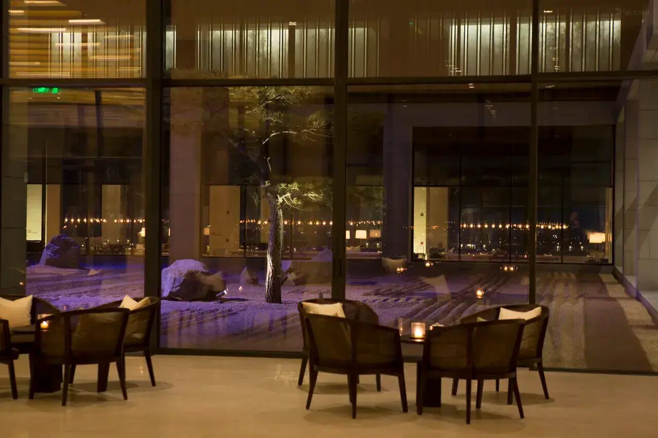 A dining area with tables and chairs, a large window with a view of a landscaped area and city lights.