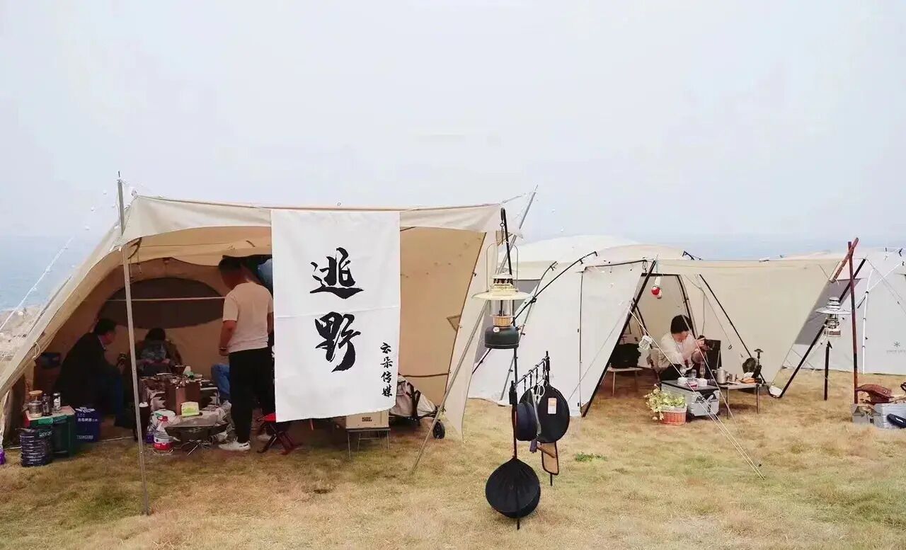 A campsite with tents and a flag, some people inside, and camping gear on the ground.