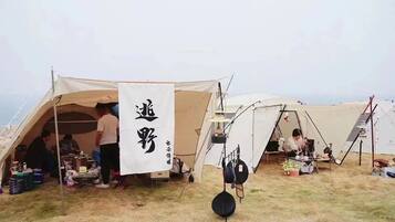 A campsite with tents and a flag, some people inside, and camping gear on the ground.