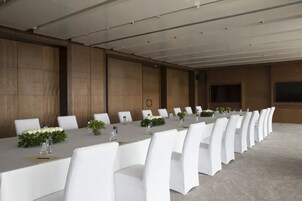 A conference room with a long table, white chairs, and a wooden panel wall.