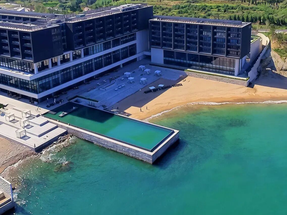 A modern hotel with a rooftop pool, a beach area, and a large building with multiple floors.