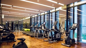 A gym with multiple cardio machines, weightlifting equipment, and a wooden floor. - The Lalu Qingdao (Qingdao)