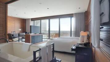 Een hotelkamer met een groot bed, een zithoek met een bureau en stoel, een badkuip en een televisietoestel.