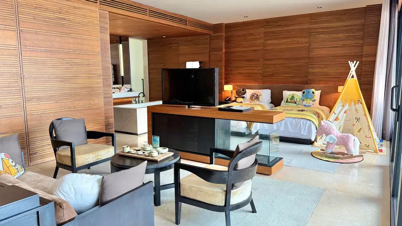Ein modernes Hotelzimmer mit Fernseher, einer Couch, Sesseln, einem Schreibtisch und einem Bett mit einer Zeltdeko.