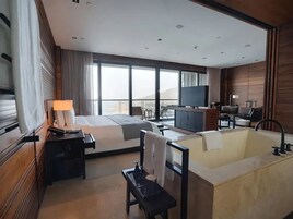 Una habitación de hotel moderna con una cama grande, una zona de estar, un televisor y una bañera.