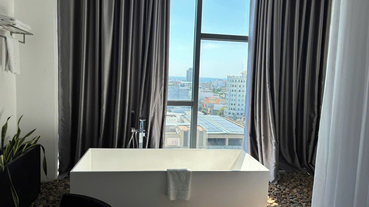 A modern bathroom with a bathtub, a towel, and a view of the cityscape through large windows.