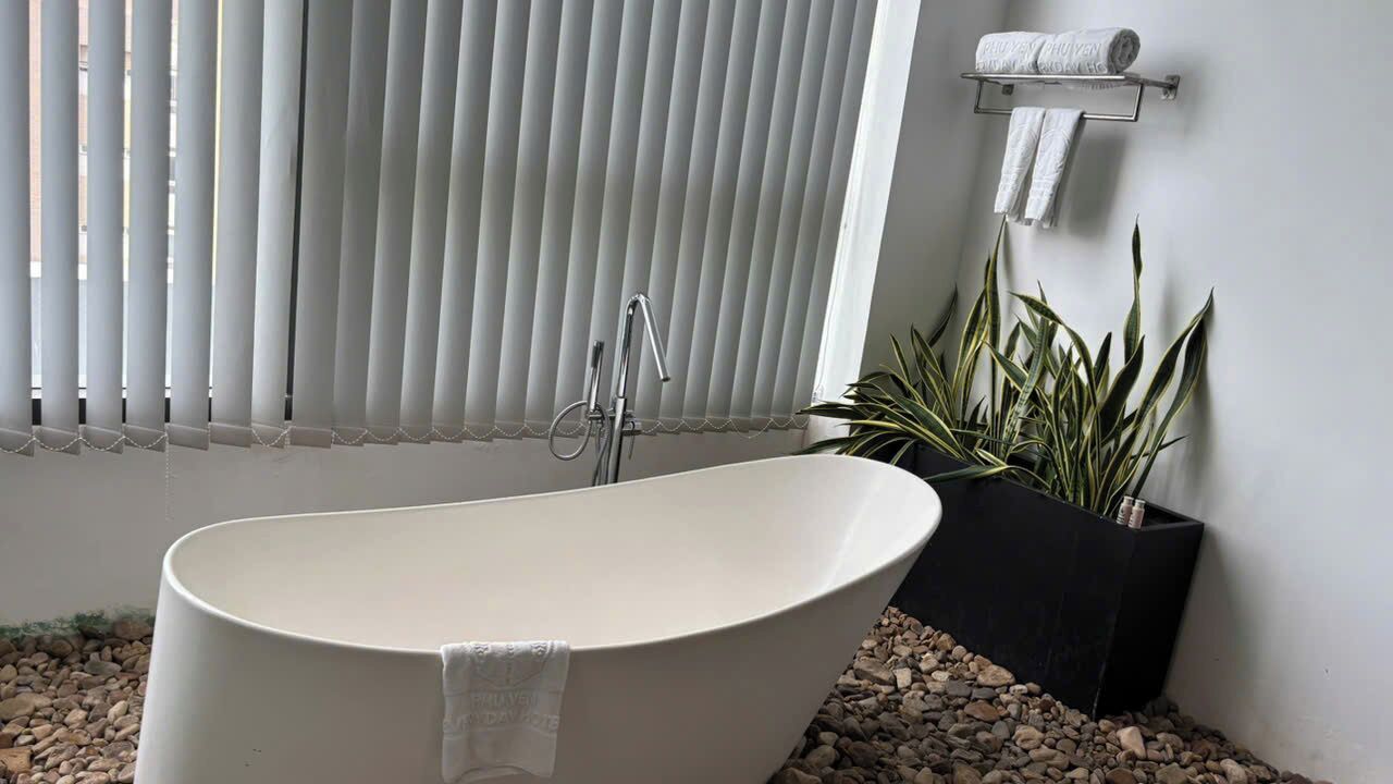 Un baño moderno con una bañera independiente, un perchero y una planta en maceta.