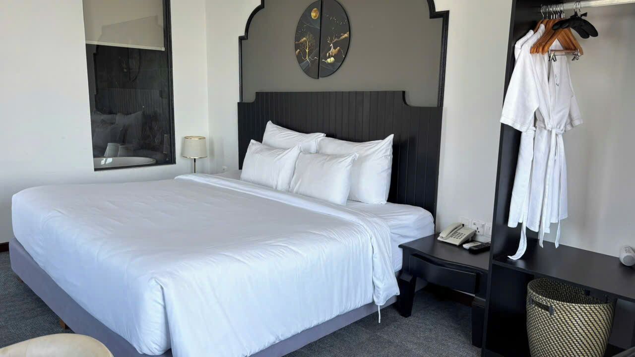 Een hotelkamer met een groot bed, een nachtkastje met een telefoon, een spiegel en een kledingkast met kleren.