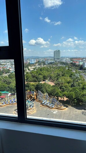 Vista desde una ventana sobre un parque con juegos infantiles y un paisaje urbano al fondo.