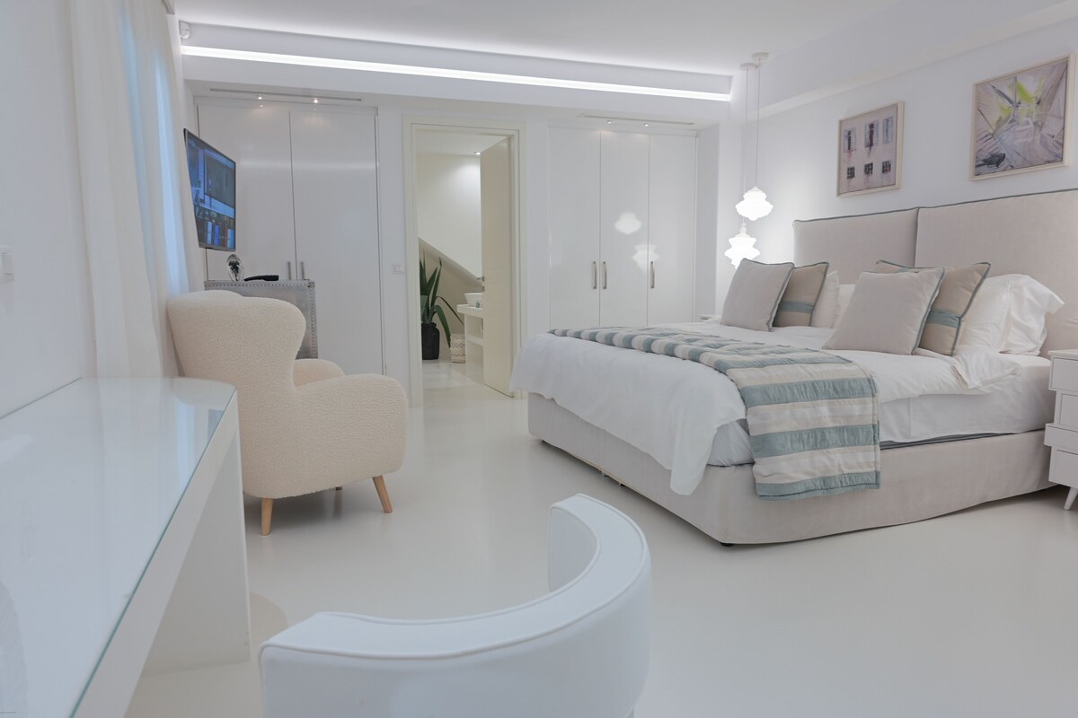 A modern bedroom with a bed, bedside tables, a chair, and a desk.