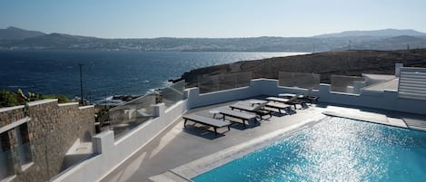 A pool area with lounge chairs and a view of the sea.