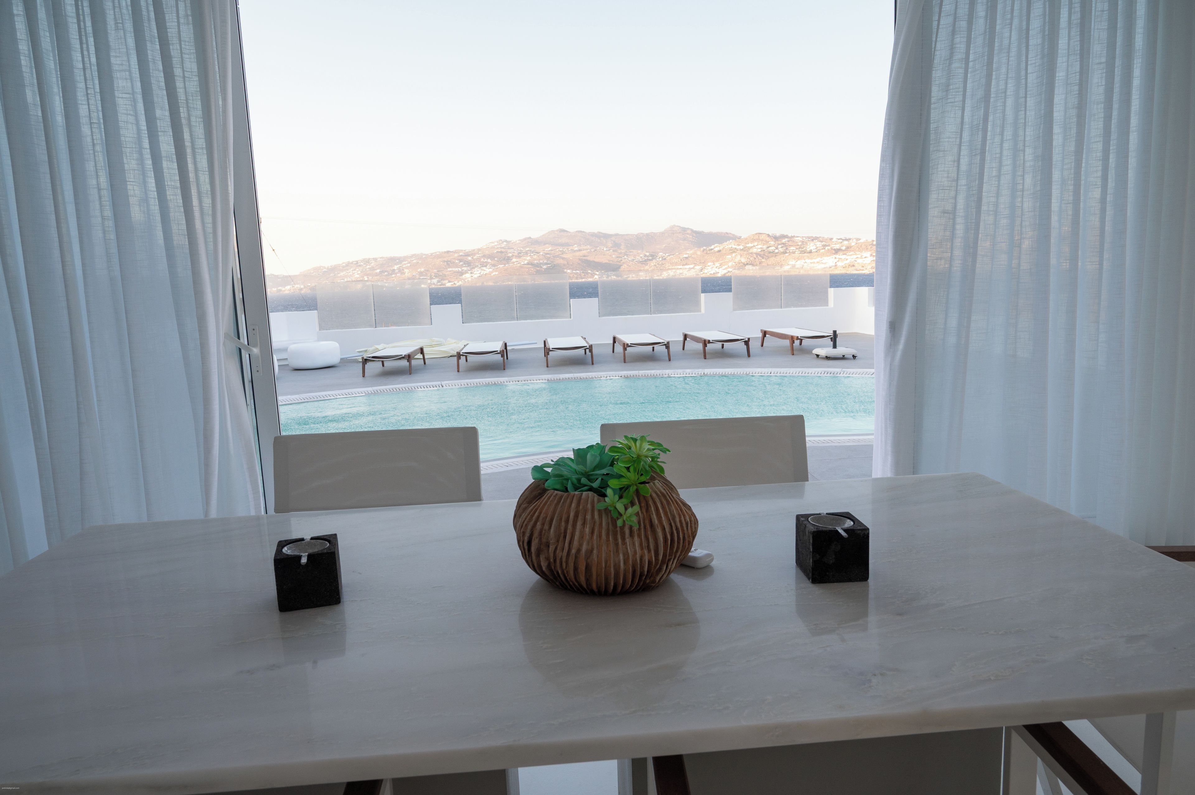 Ein Zimmer mit Blick auf einen Pool und Stühle, ein Tisch mit einer Pflanze und ein Fenster mit Vorhängen.