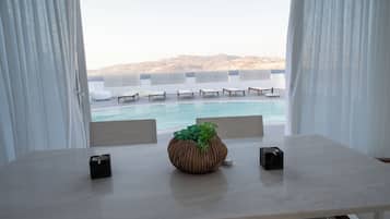 Ein Zimmer mit Blick auf einen Pool und Stühle, ein Tisch mit einer Pflanze und ein Fenster mit Vorhängen.