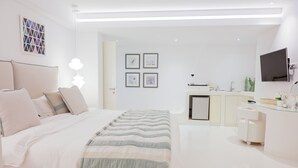 Un dormitorio moderno con cama, mesitas de noche, lámpara de noche, televisor montado en la pared y una pequeña kitchenette.