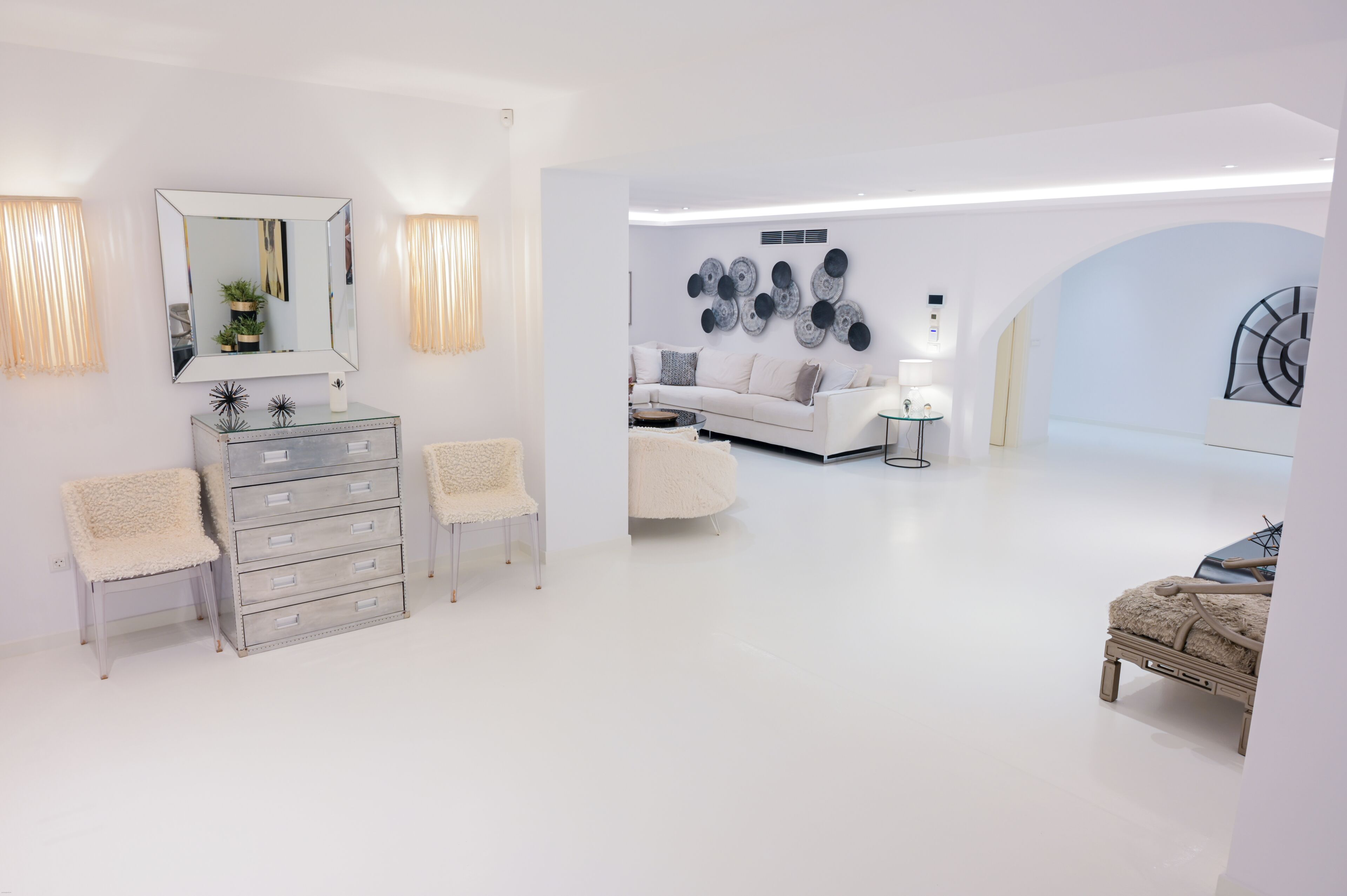 Un intérieur moderne aux couleurs claires, avec un canapé, une commode et des œuvres d’art décoratives au mur.