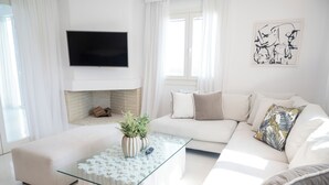 Una sala de estar moderna con una mesa de centro de vidrio, sofás blancos, un televisor de pantalla plana y una chimenea.
