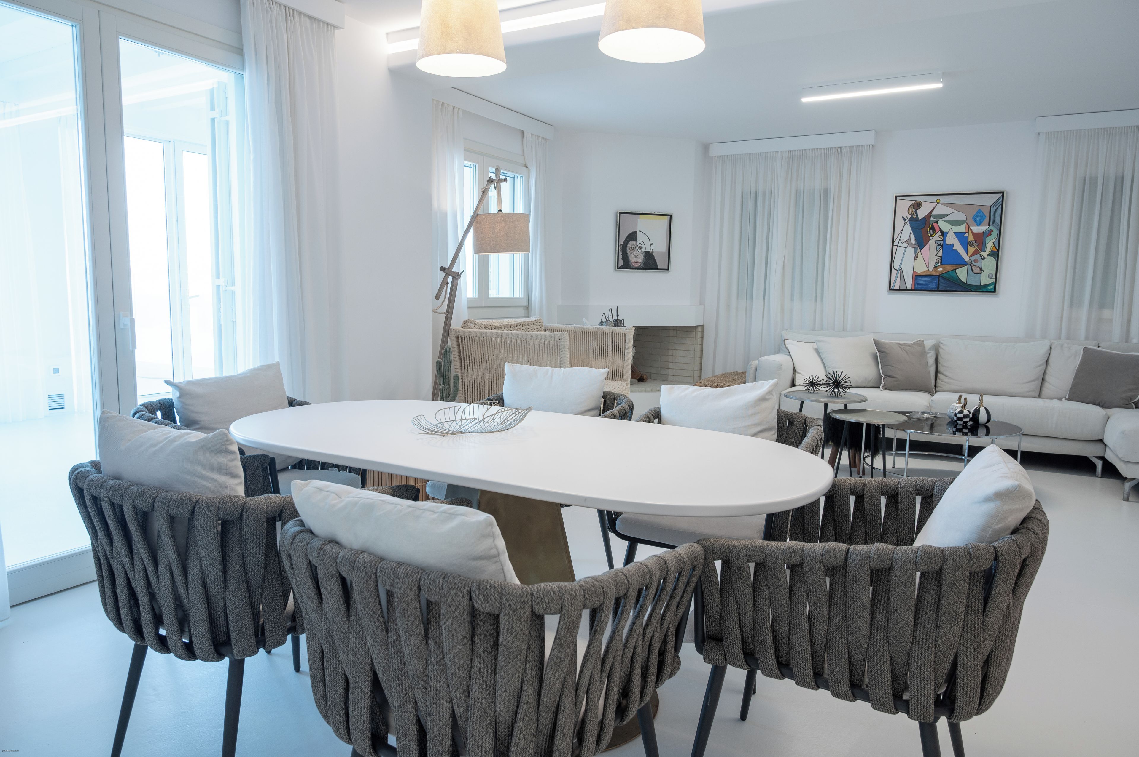 A modern living room with a white sofa, grey armchairs, a round dining table, and a fireplace.