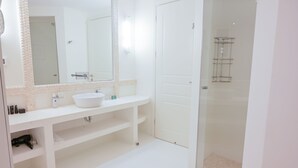 Un baño con lavamanos blanco, espejo y zona de ducha.