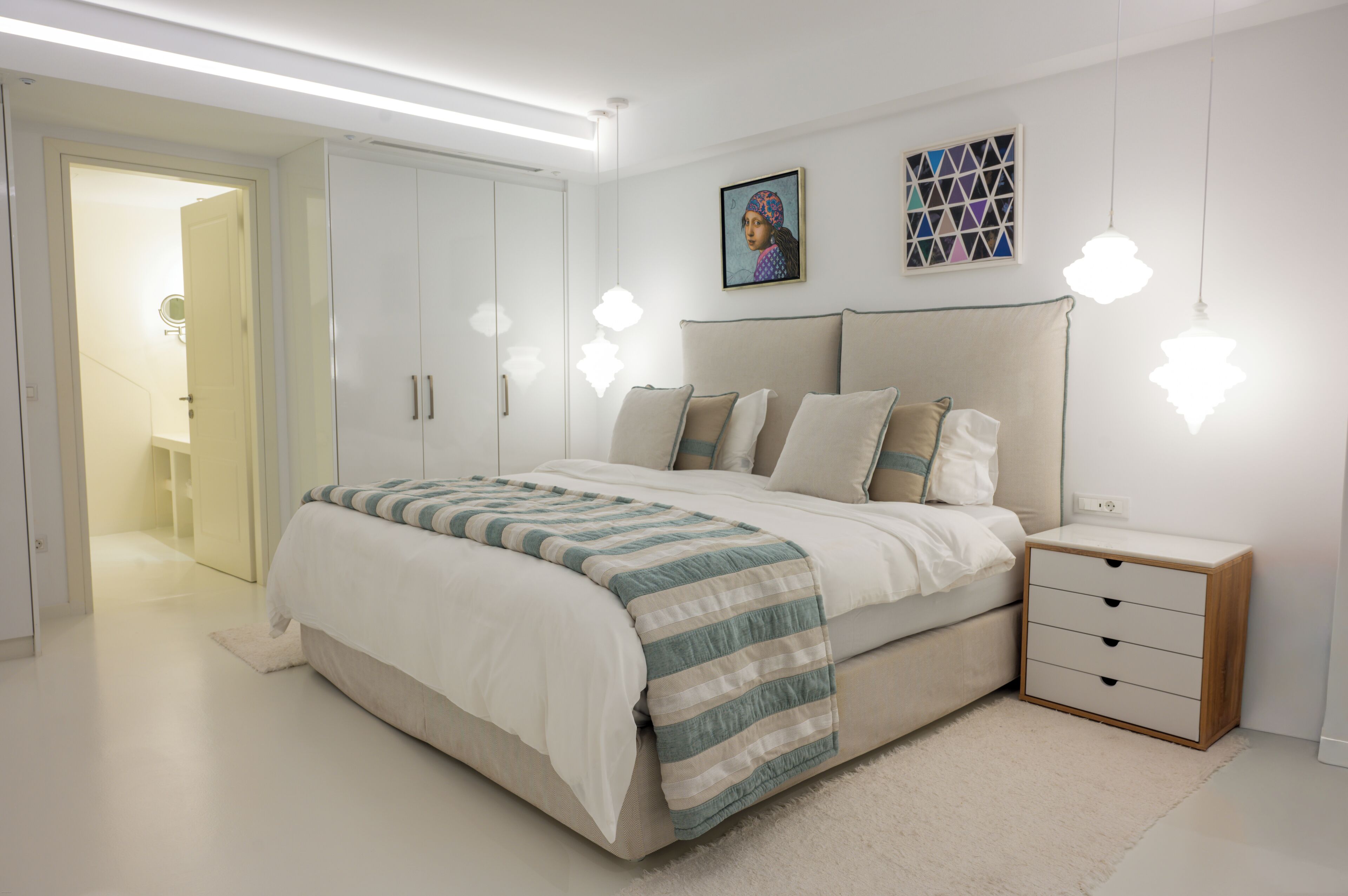 Un dormitorio moderno con una cama grande, mesitas de noche, un armario y un cuadro en la pared.