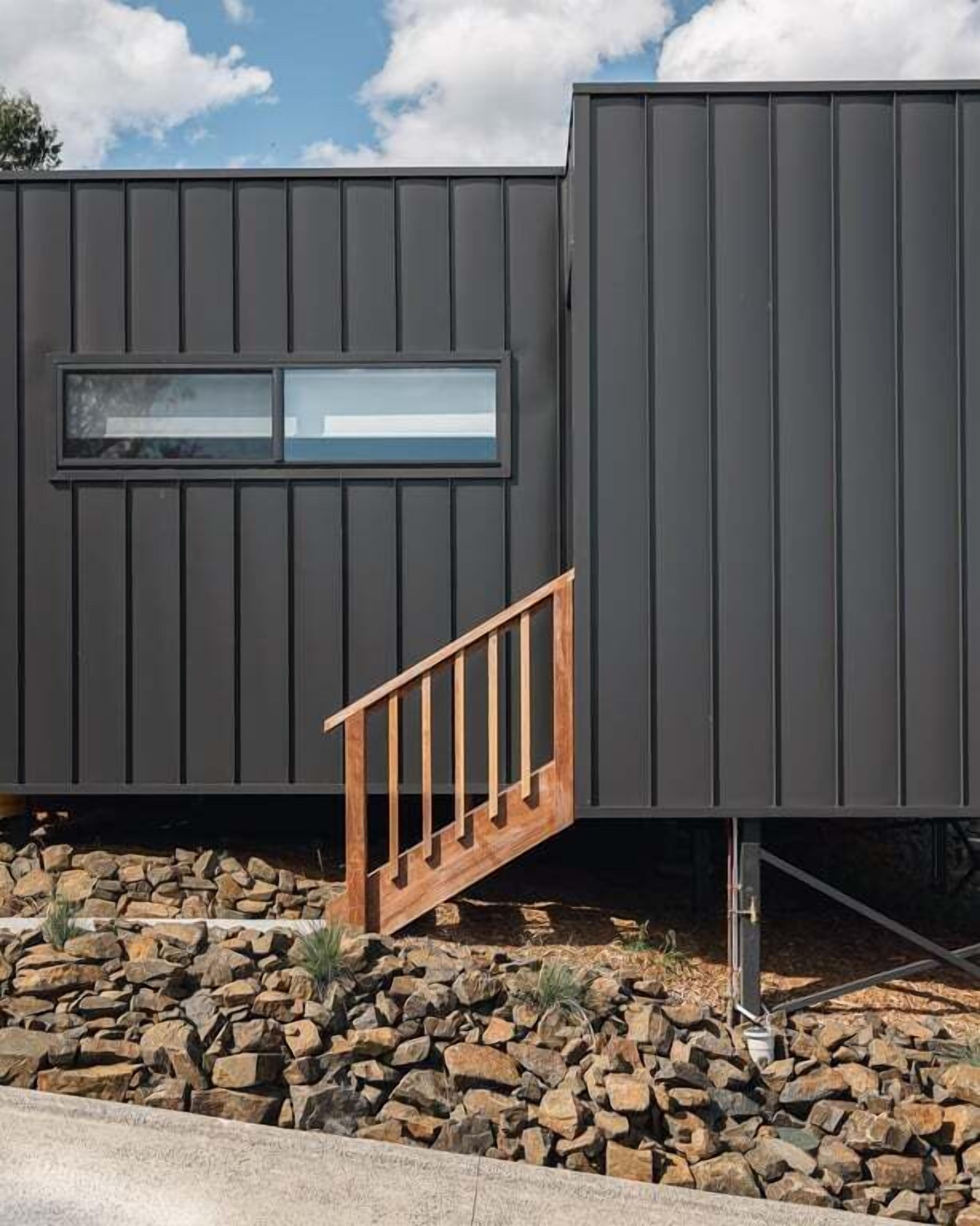 A modern building with a dark exterior, a wooden staircase, and a window.