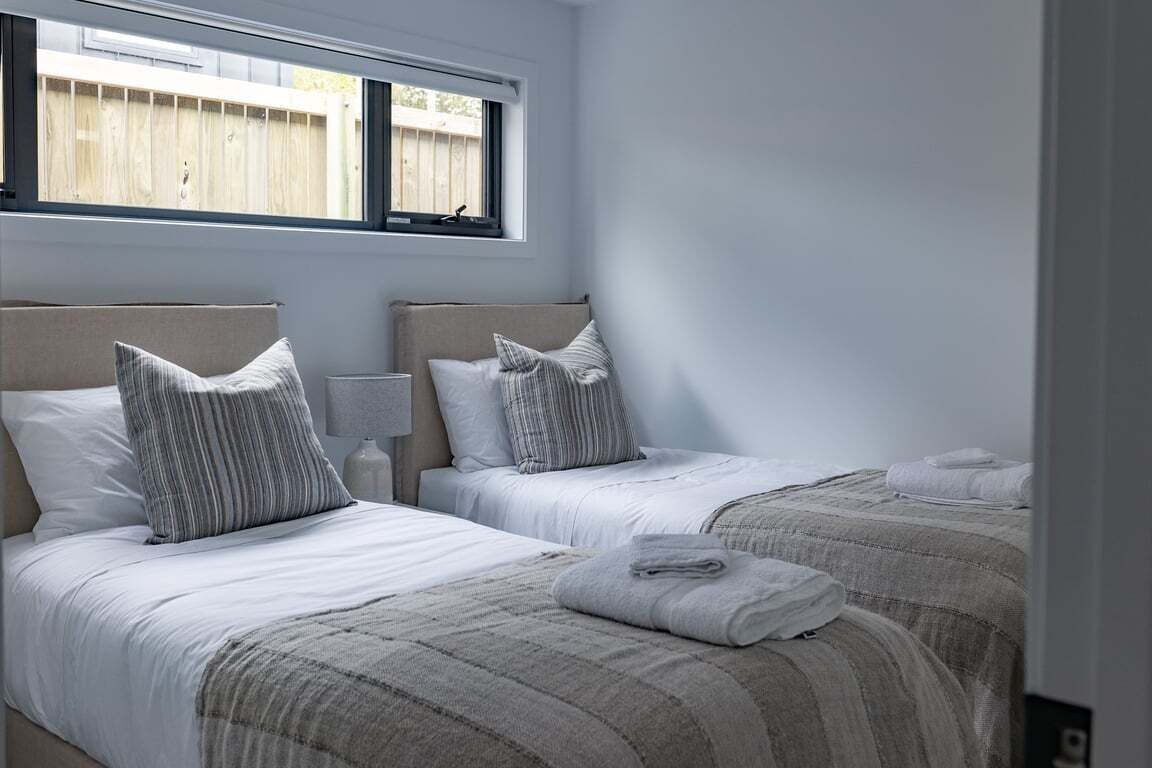A bedroom with two beds, each with a headboard, a bedside table, and a window.