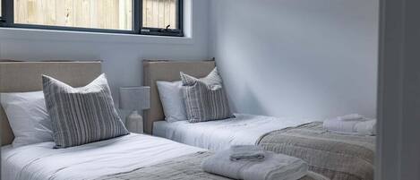 A bedroom with two beds, each with a headboard, a bedside table, and a window.
