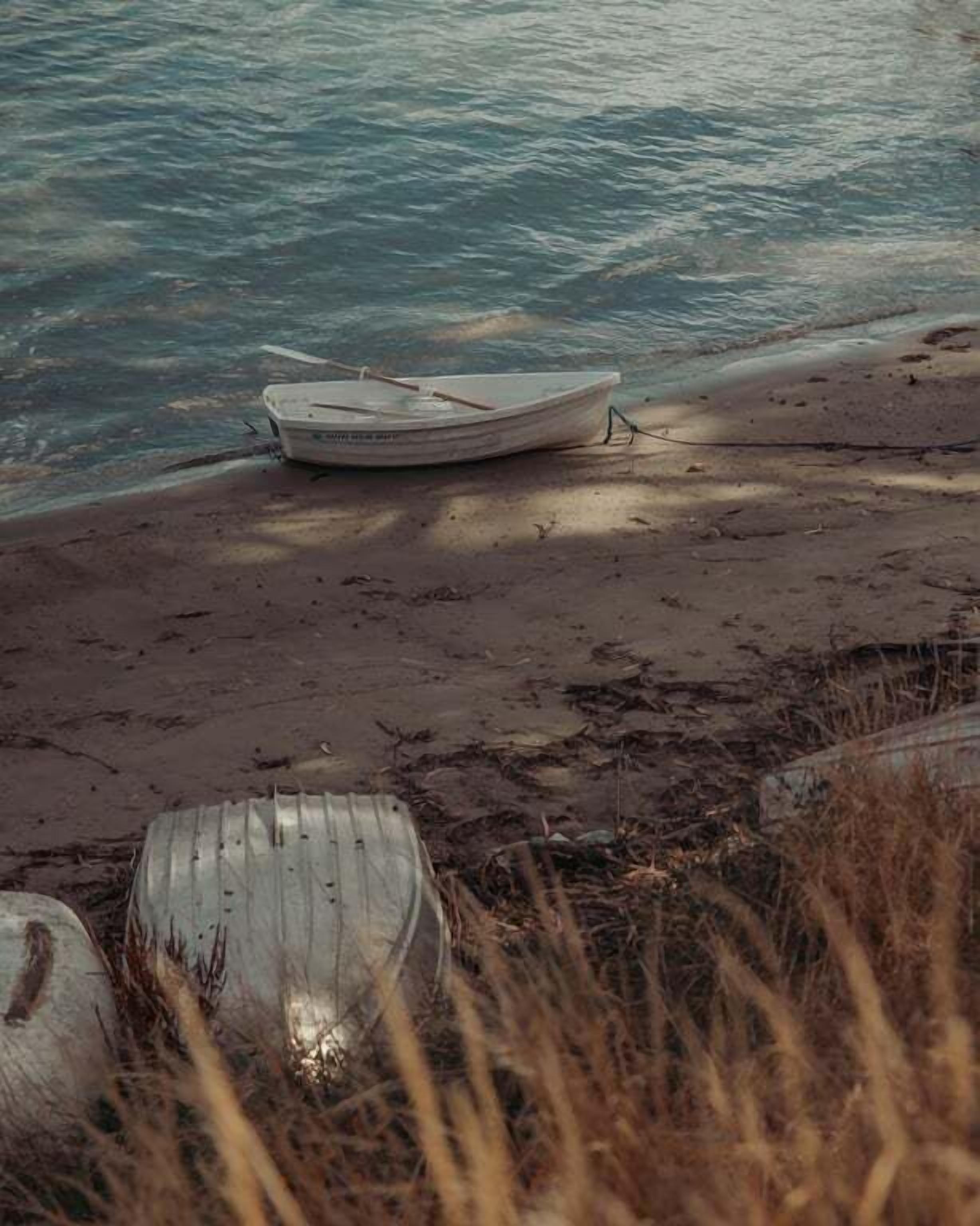 A boat on a sandy beach with water in the background.