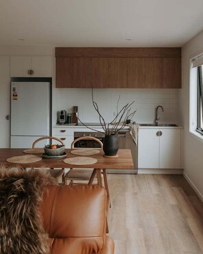 A modern kitchen with wooden cabinets, a white countertop, and a dining area with a table and chairs.