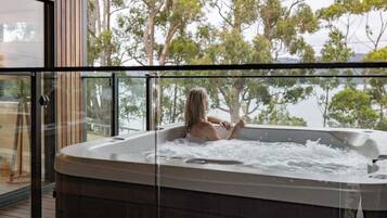 A person relaxing in a hot tub with a view of trees and a body of water.