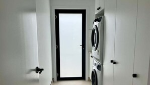 A laundry room with a washing machine and dryer, a tiled floor, and a door leading to another room. - Ocean Mist Cabin – Spa, Fireplace & EV Charger (Huon Valley)