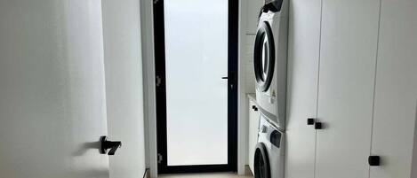 A laundry room with a washing machine and dryer, a tiled floor, and a door leading to another room.