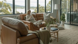 A modern living room with a leather sofa, a coffee table, and a view of the outdoors. - Ocean Mist Cabin – Spa, Fireplace & EV Charger (Huon Valley)