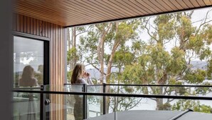 A modern interior with a glass balcony overlooking a natural landscape. - Ocean Mist Cabin – Spa, Fireplace & EV Charger (Huon Valley)