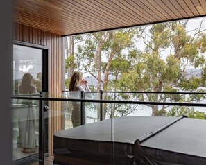 A modern interior with a glass balcony overlooking a natural landscape. - Ocean Mist Cabin – Spa, Fireplace & EV Charger (Huon Valley)