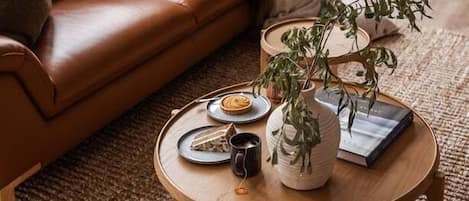 A cozy living room with a brown leather sofa, a round wooden coffee table with a plant, a book, and a mug.