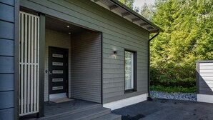 Ein modernes Haus mit grauem Anstrich, einer schwarzen Tür mit mehreren Feldern und einer kleinen Veranda mit Stufen zum Eingang.