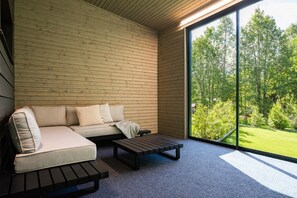 Ein modernes Interieur mit einer Holzwand, einem Sofa, einem Couchtisch und einer großen Glasschiebetür, die zu einem grünen Außenbereich führt.