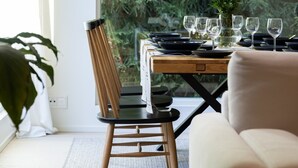 Ein Essbereich mit einem Tisch für sechs Personen, einem Stuhl, einer Couch und Blick auf einen Wald durch große Fenster.