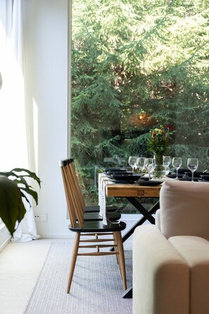 A dining area with a table set for six, a chair, a sofa, and a view of a forest through large windows. - Christmas Villa, Private Sauna By Lapland Host (Rovaniemi)