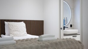 Ein modernes Schlafzimmer mit einem Bett, einem flauschigen Teppich und einem durchgegangenen Türrahmen einsehbaren Badezimmer.