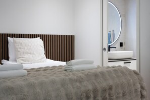 A modern bedroom with a bed, a fluffy rug, and a bathroom visible through an open door. - Christmas Villa, Private Sauna By Lapland Host (Rovaniemi)